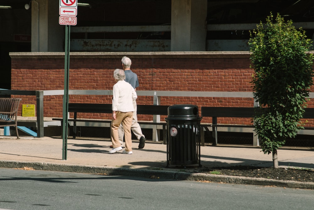 a man walking down a sidewalk next to a trash can