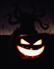 A carved pumpkin with an eerie, menacing face is illuminated from within. In the background, a dark, shadowy figure with tentacle-like appendages is silhouetted against a dimly lit sky.