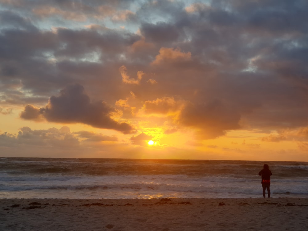 a person standing on the beach watching the sun set