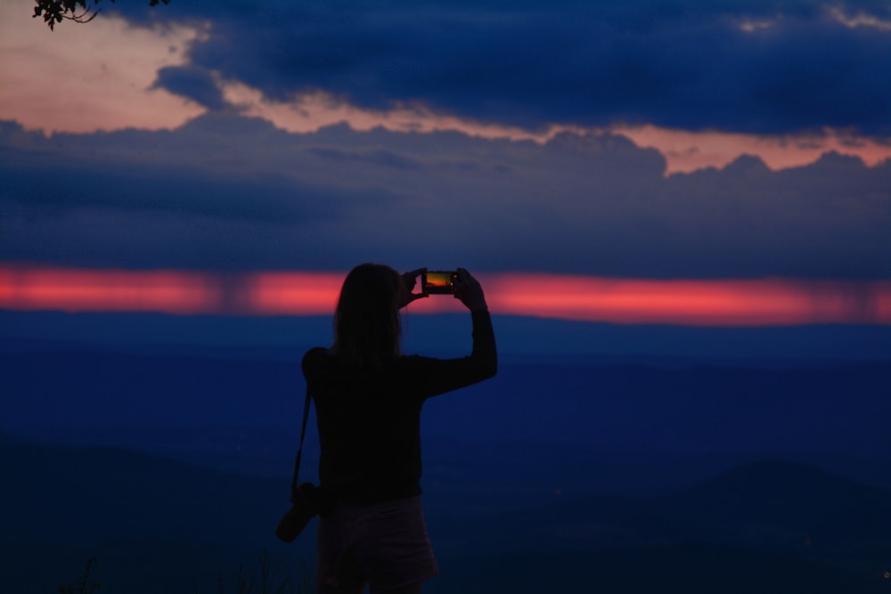 a woman taking a picture of a sunset with her cell phone