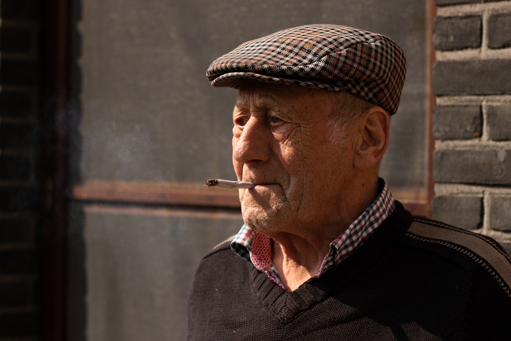 an old man smoking a cigarette in front of a brick wall