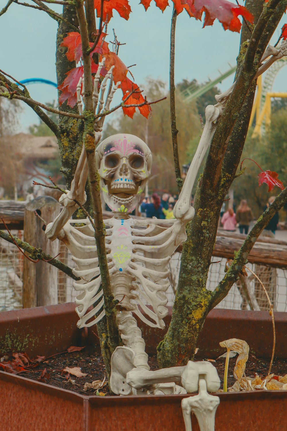 um esqueleto sentado em um vaso de flores ao lado de uma árvore