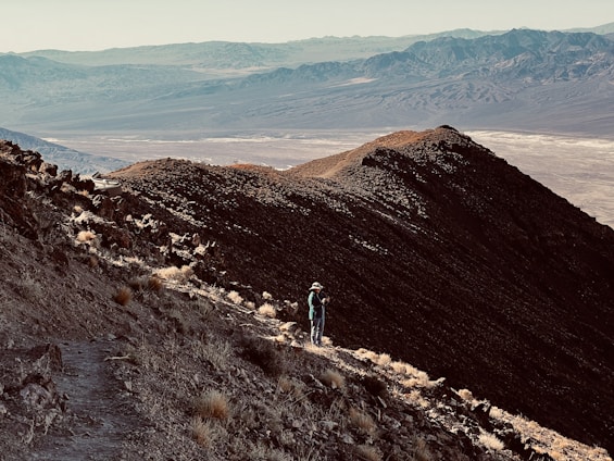 A panoramic view of a hiker standing on a mountain peak overlooking a vast, sunlit valley.