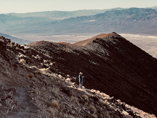 A lone hiker standing on a rocky cliff overlooking a vast desert landscape at sunset
