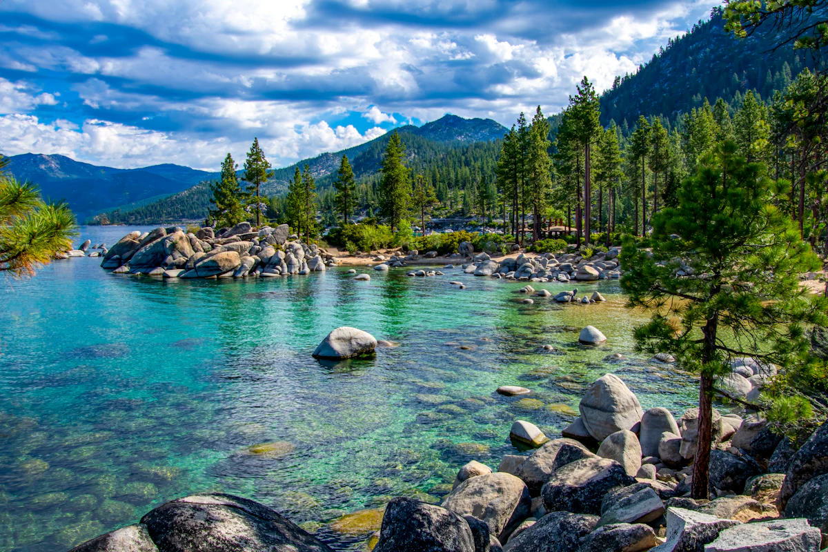 Granite boulders in clear turquoise water at Sand Harbor, on the Nevada shore of Lake Tahoe, with pines and a forested peak behind