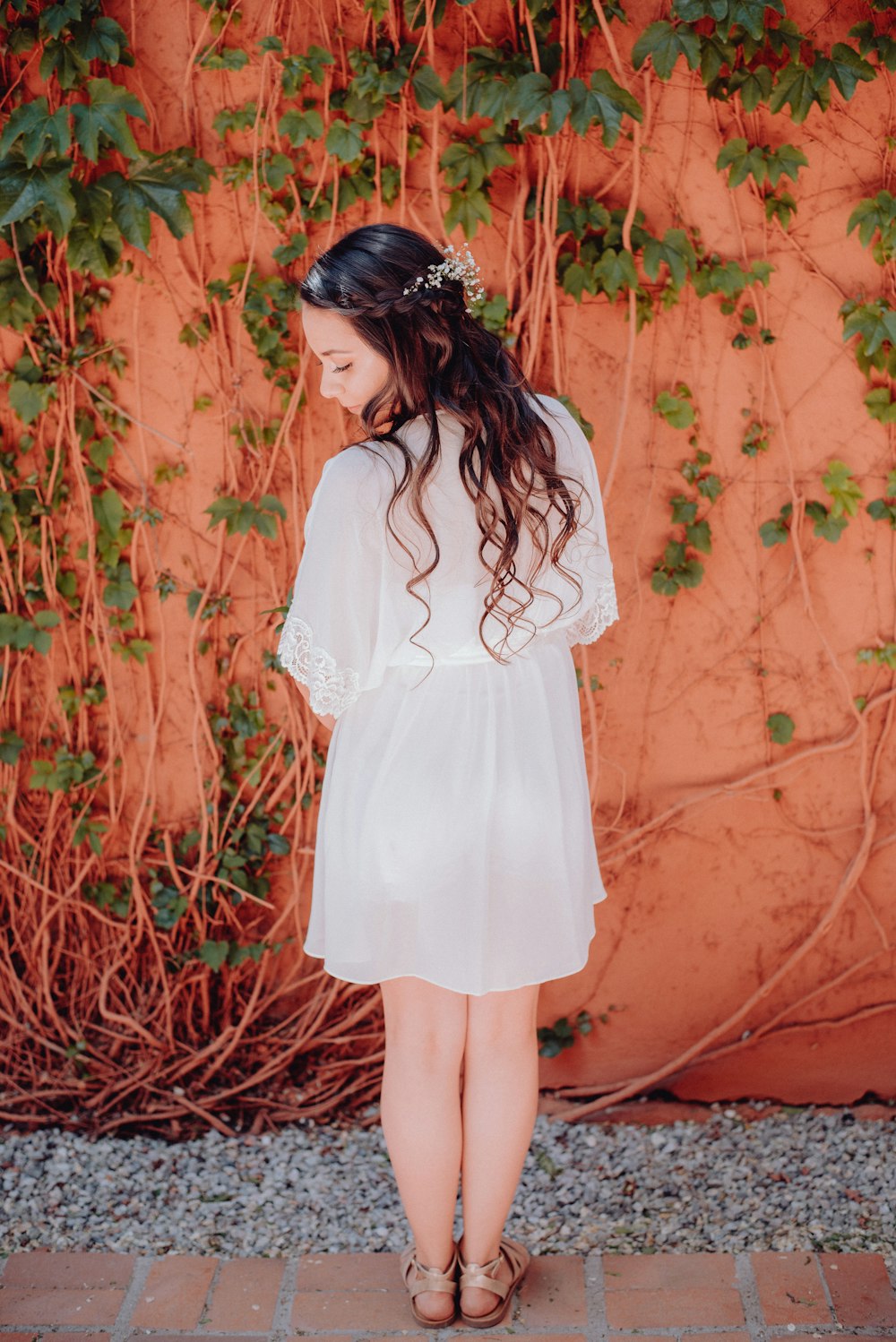 a woman standing in front of a wall wearing a white dress