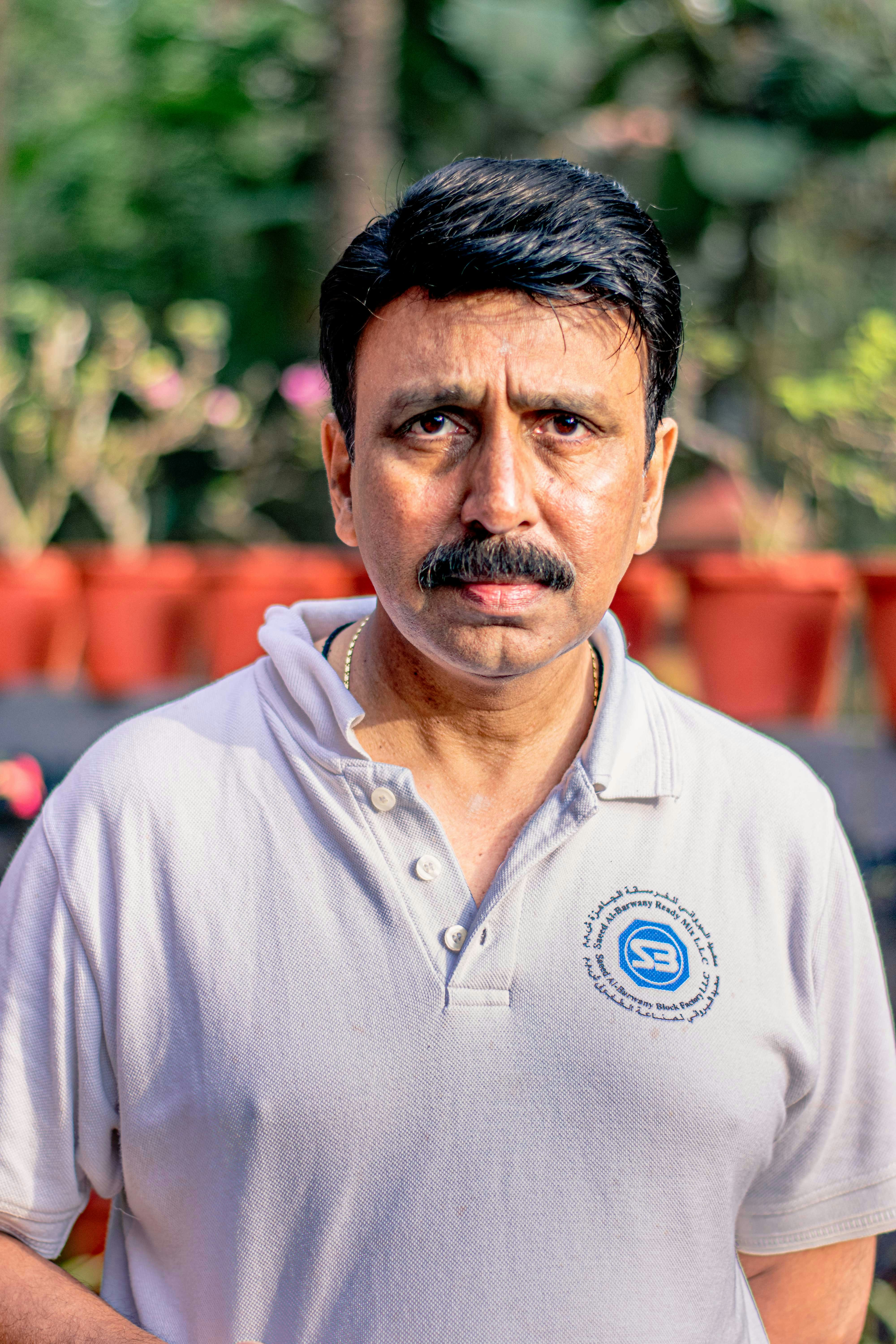 a man with a mustache standing in front of potted plants