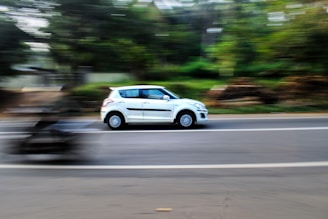 a white car driving down a street next to a forest