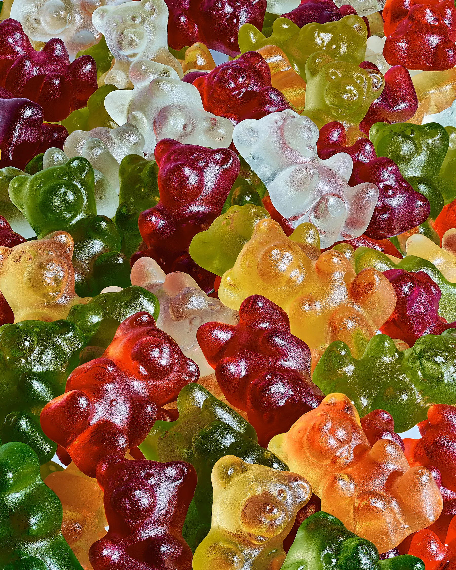 Close-up of glossy red, green, clear and orange gummy bears piled together