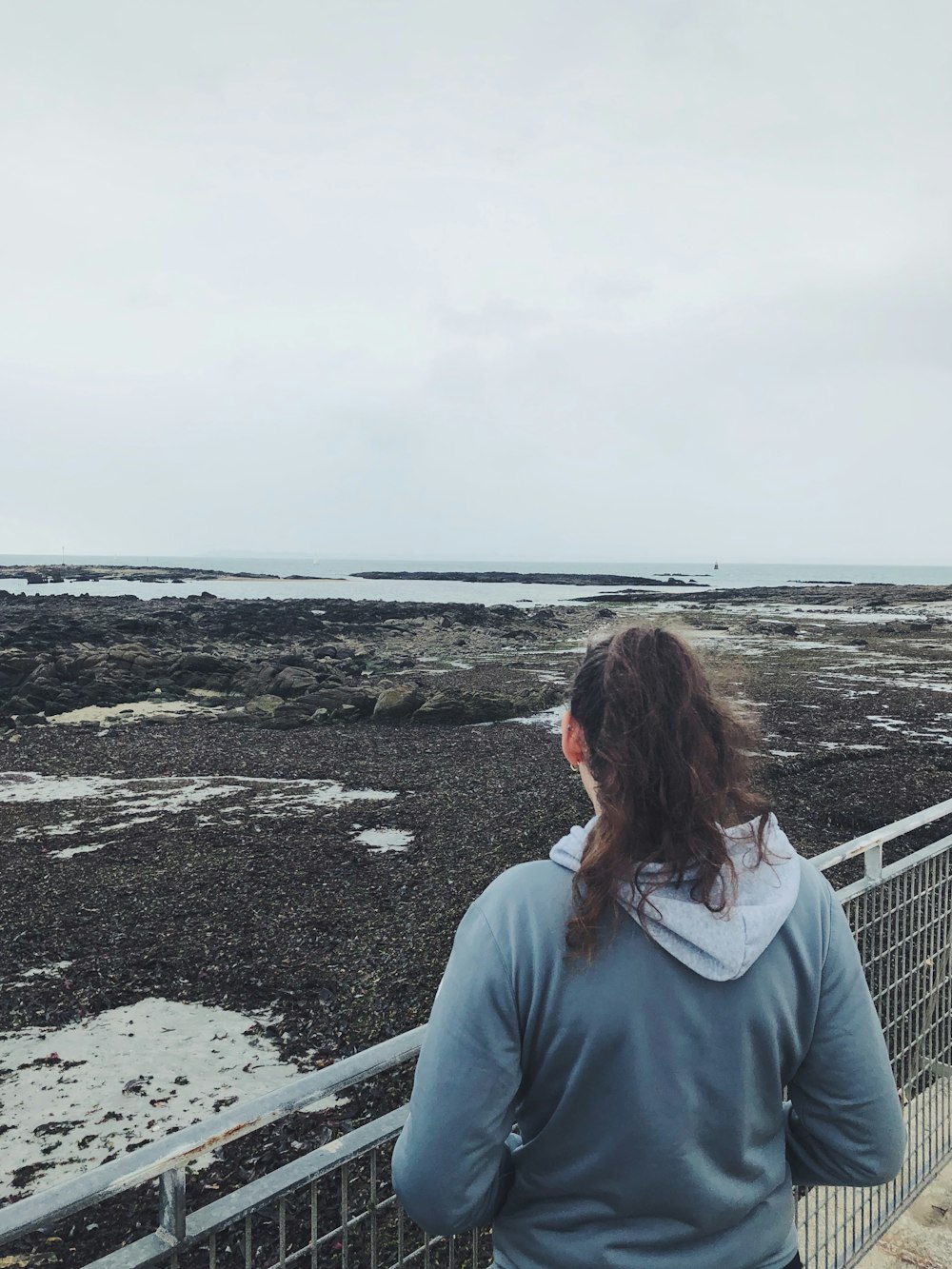 a woman standing on a bridge looking out at the ocean