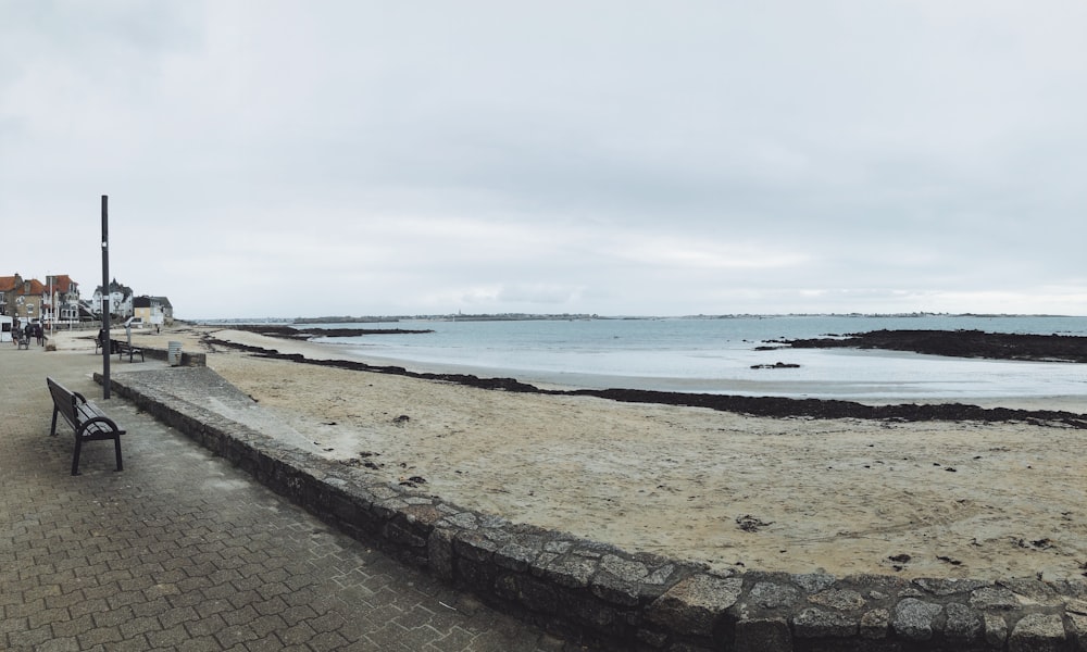 a bench sitting on the side of a beach next to the ocean