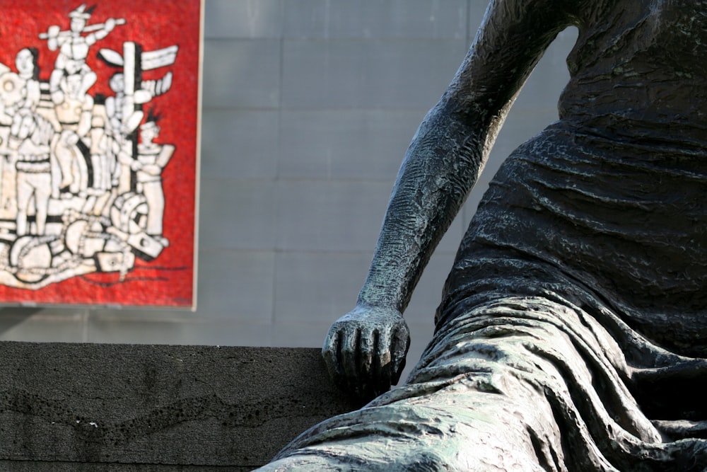 una statua di una donna seduta sulla cima di un muro di cemento