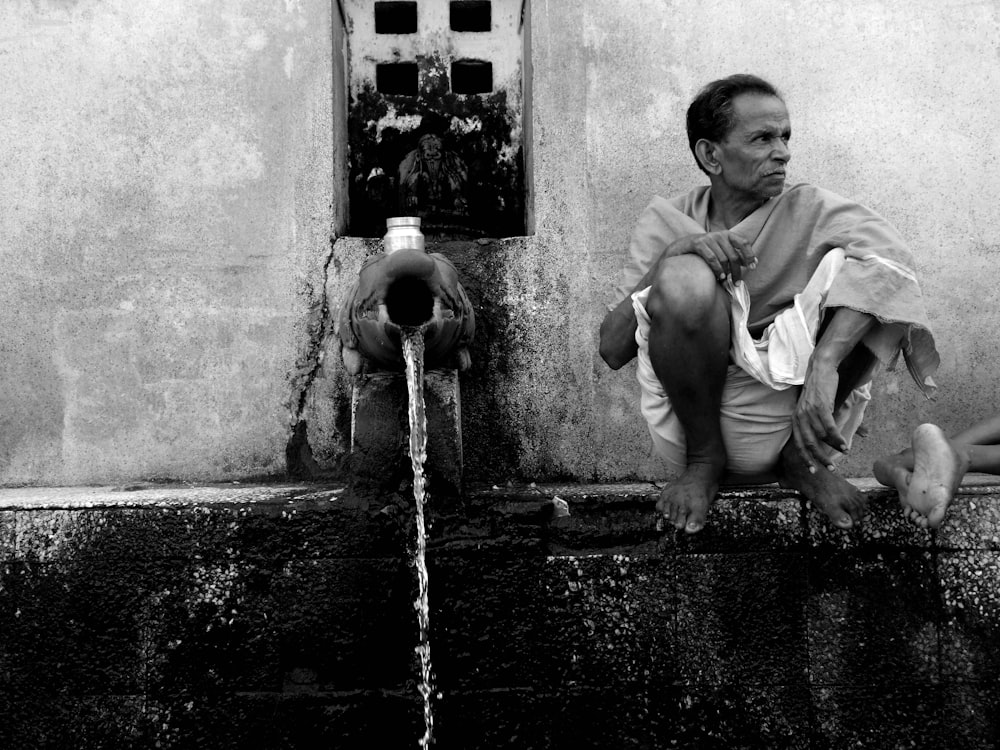 a black and white photo of a man sitting next to a fire hydrant