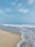 A serene beach scene with soft white sand and gentle waves under a clear blue sky.