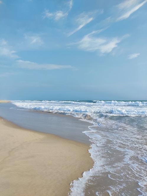 A serene beach scene under a bright blue sky with gentle waves and summer sunlight.