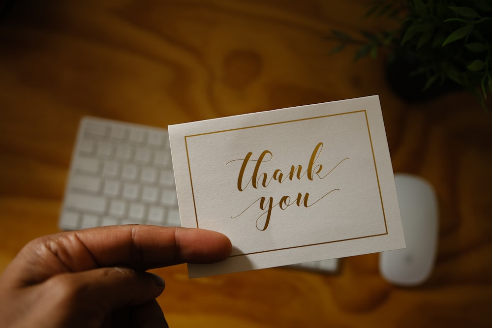 a person holding a thank you card in front of a keyboard