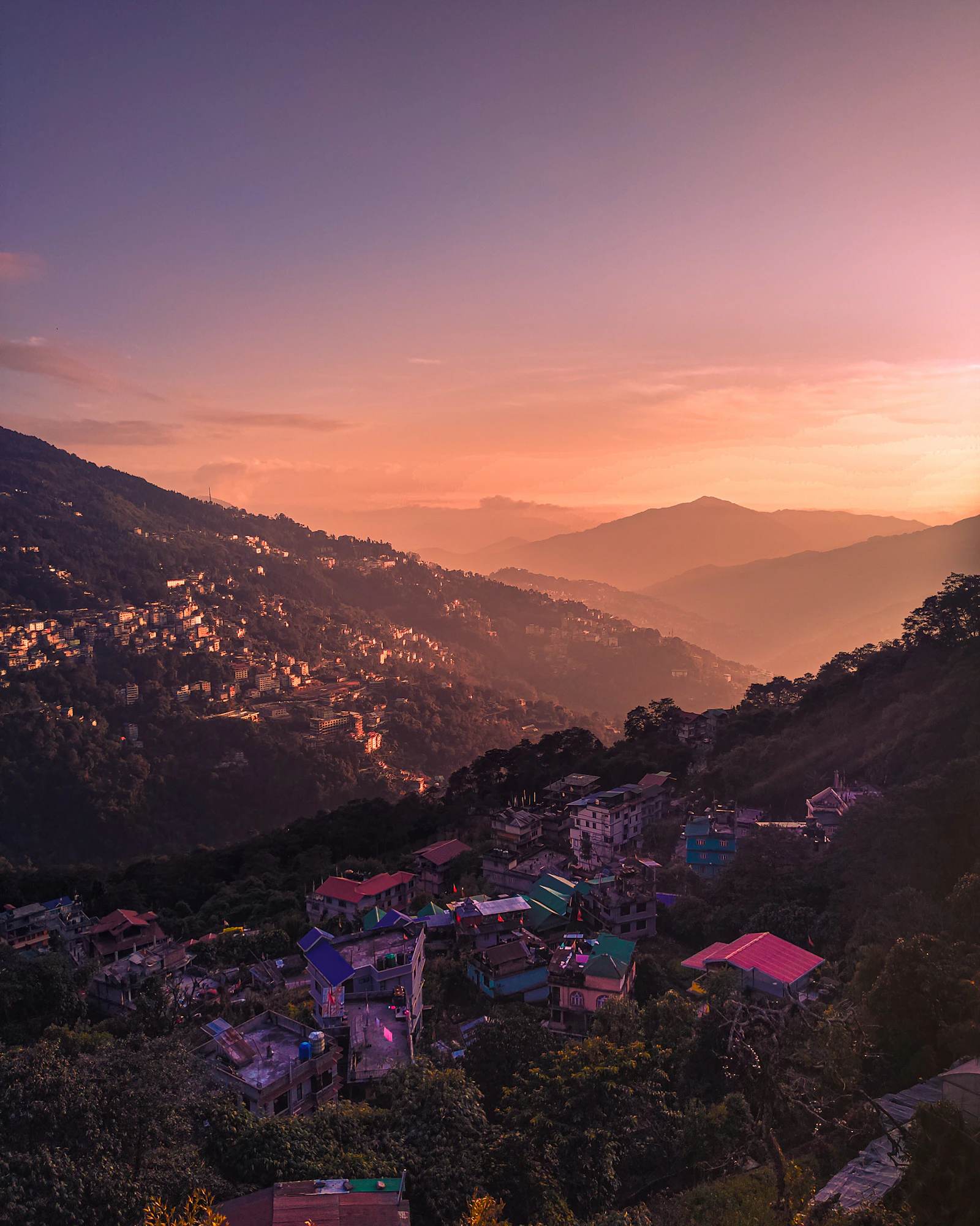 Gangtok's houses spread along a forested ridge under a rose and amber sky, the hills of East Sikkim fading into the distance