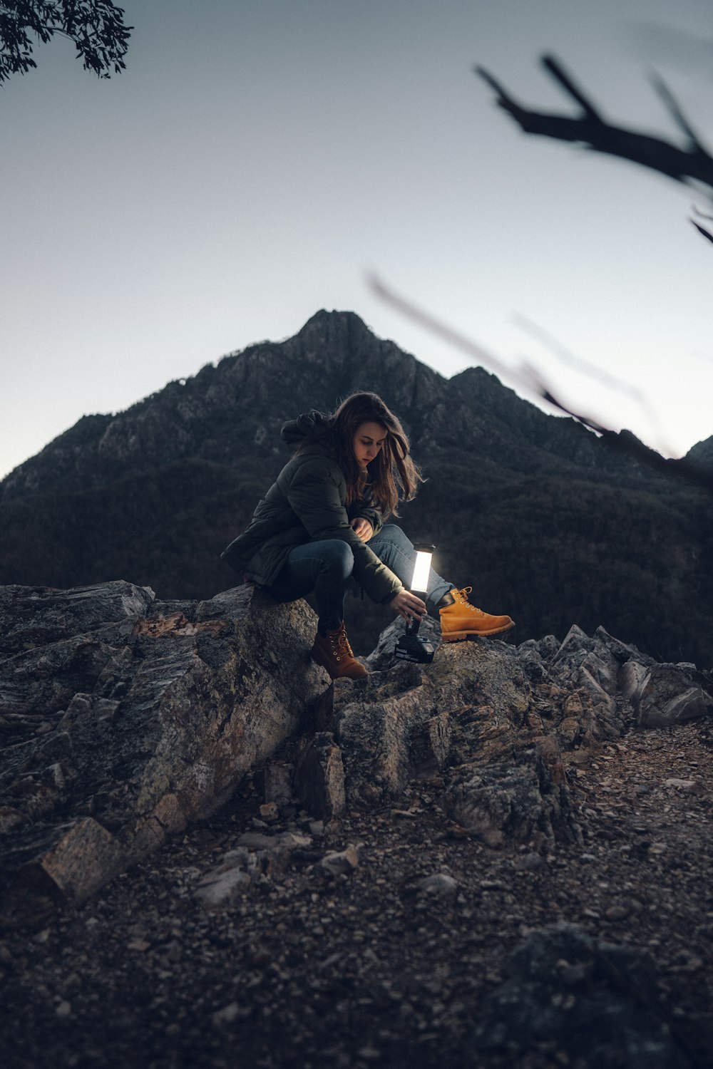 a woman sitting on a rock with a flashlight in her hand