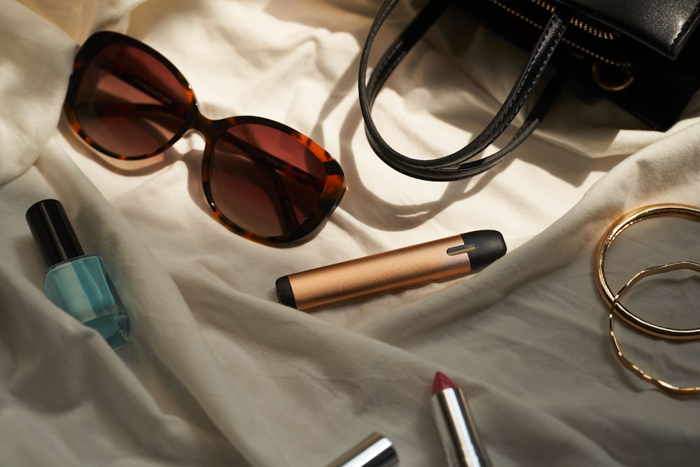 a pair of sunglasses, lipstick, and a purse on a bed