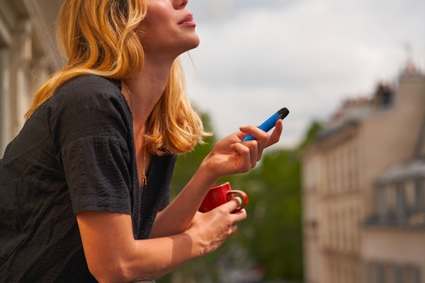 a woman holding a cup and a cell phoneby Romain B