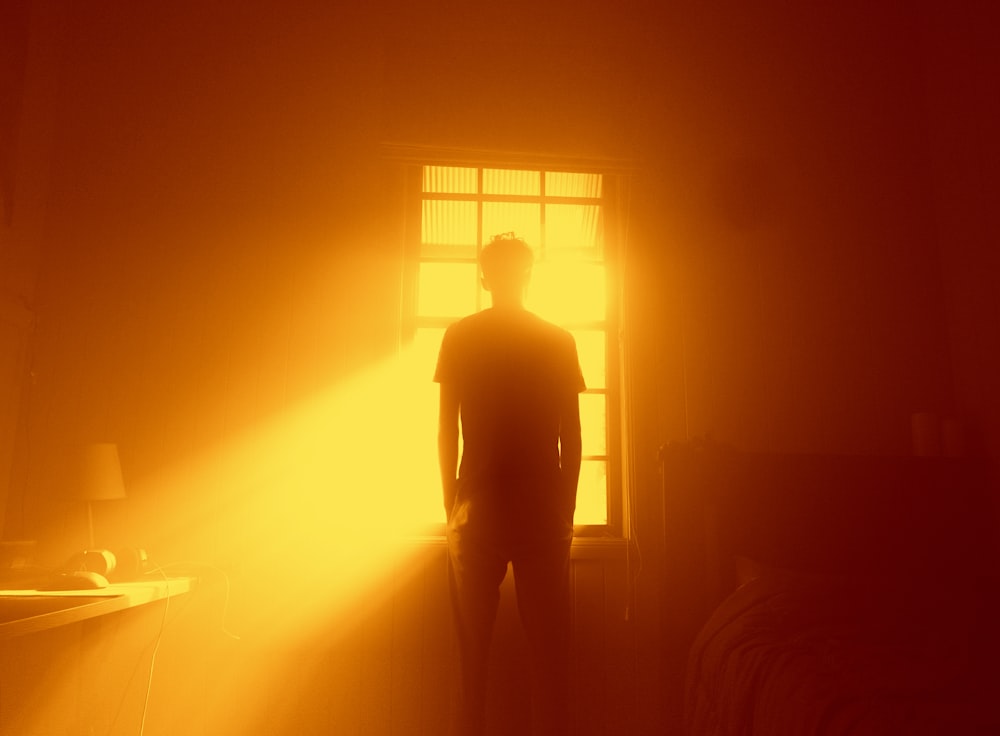 Un hombre parado frente a una ventana en la oscuridad