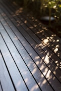 a close up of a wooden deck with plants in the background