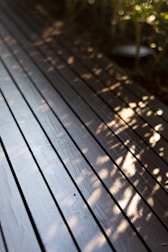 a close up of a wooden deck with plants in the background