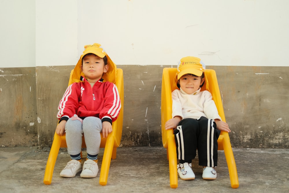 two children sitting on yellow chairs with hats on