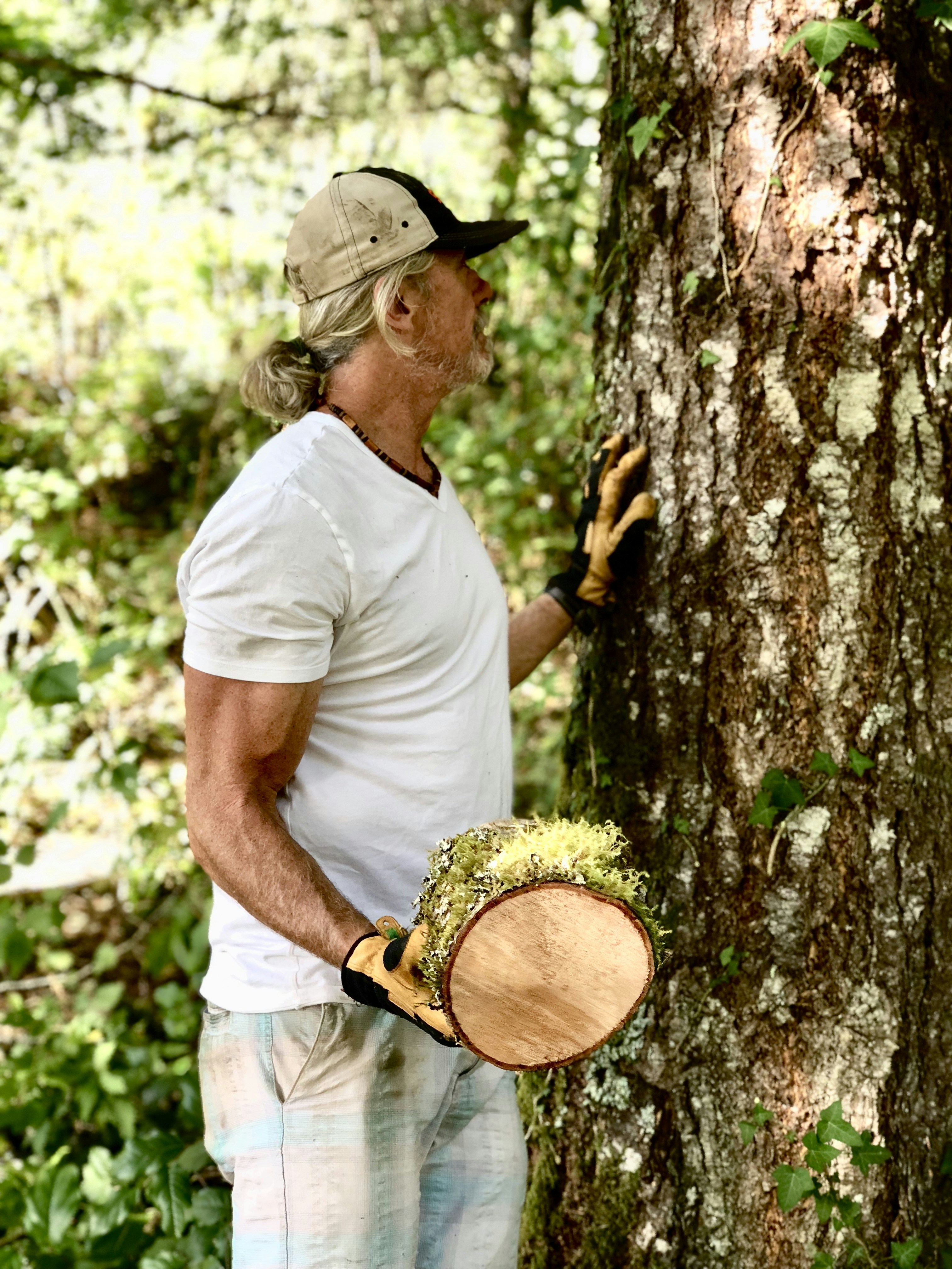 a man holding a hat and glove next to a tree