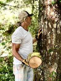 a man holding a hat and glove next to a tree