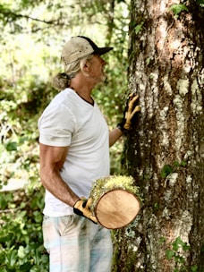 a man holding a hat and glove next to a tree
