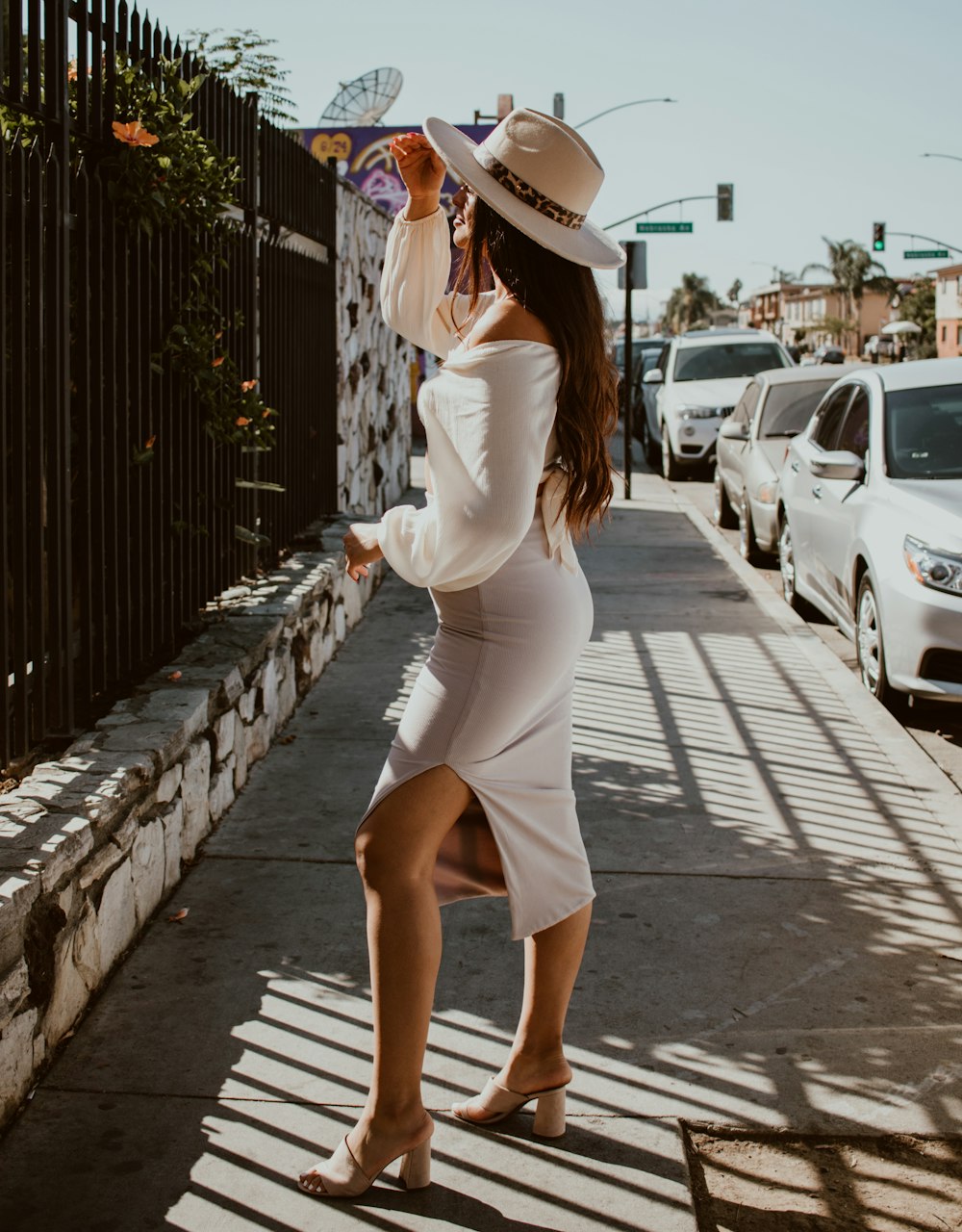 a woman in a white dress and hat walking down the street