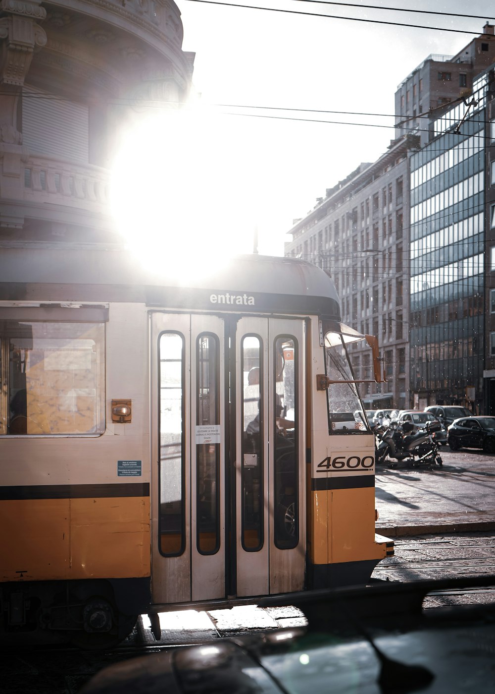 a yellow and white train traveling past tall buildings