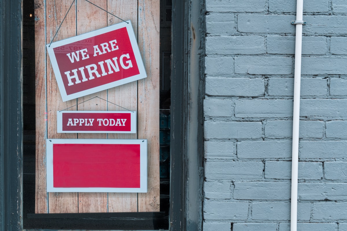 A 'We Are Hiring' sign in the window of a brick building representing the state of the American labor market