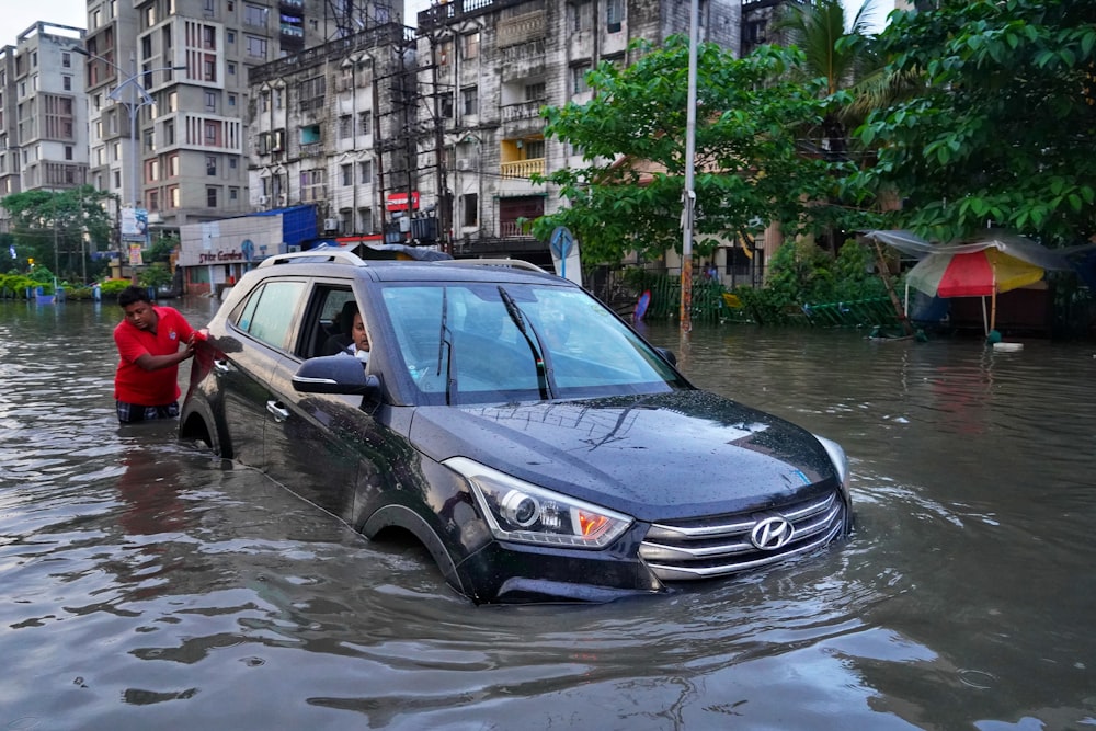 a couple of people standing next to a car in a flooded street