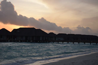 A shadowy overwater villa at dusk, lit subtly against a dark obsidian sky.