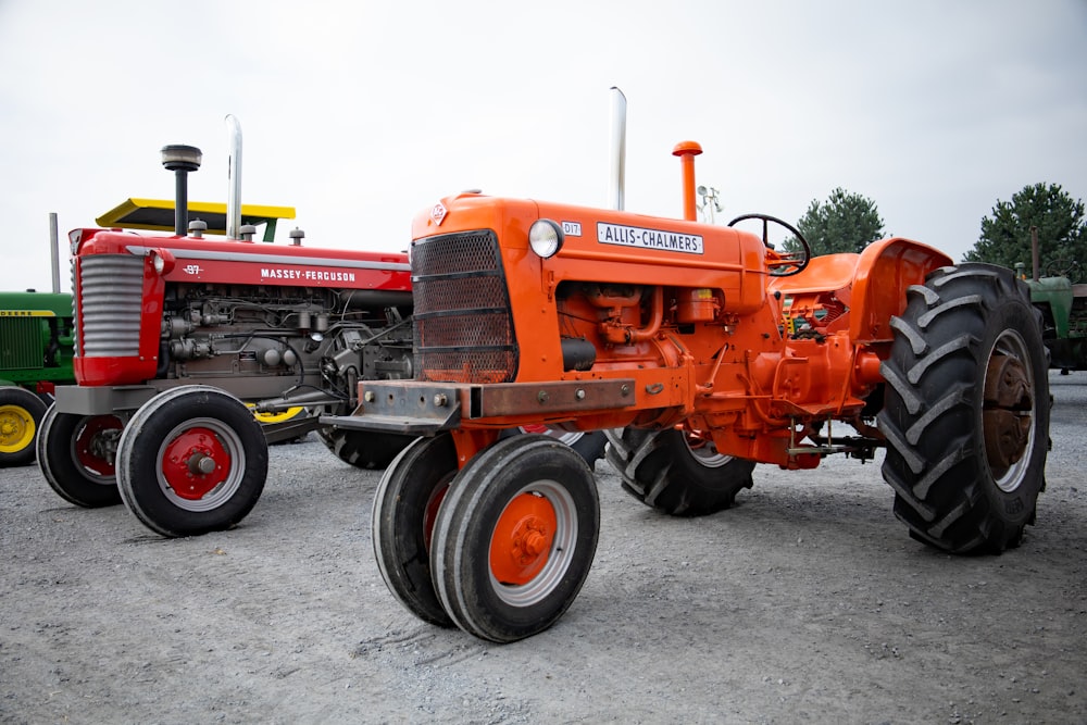 an orange tractor parked next to a green tractor