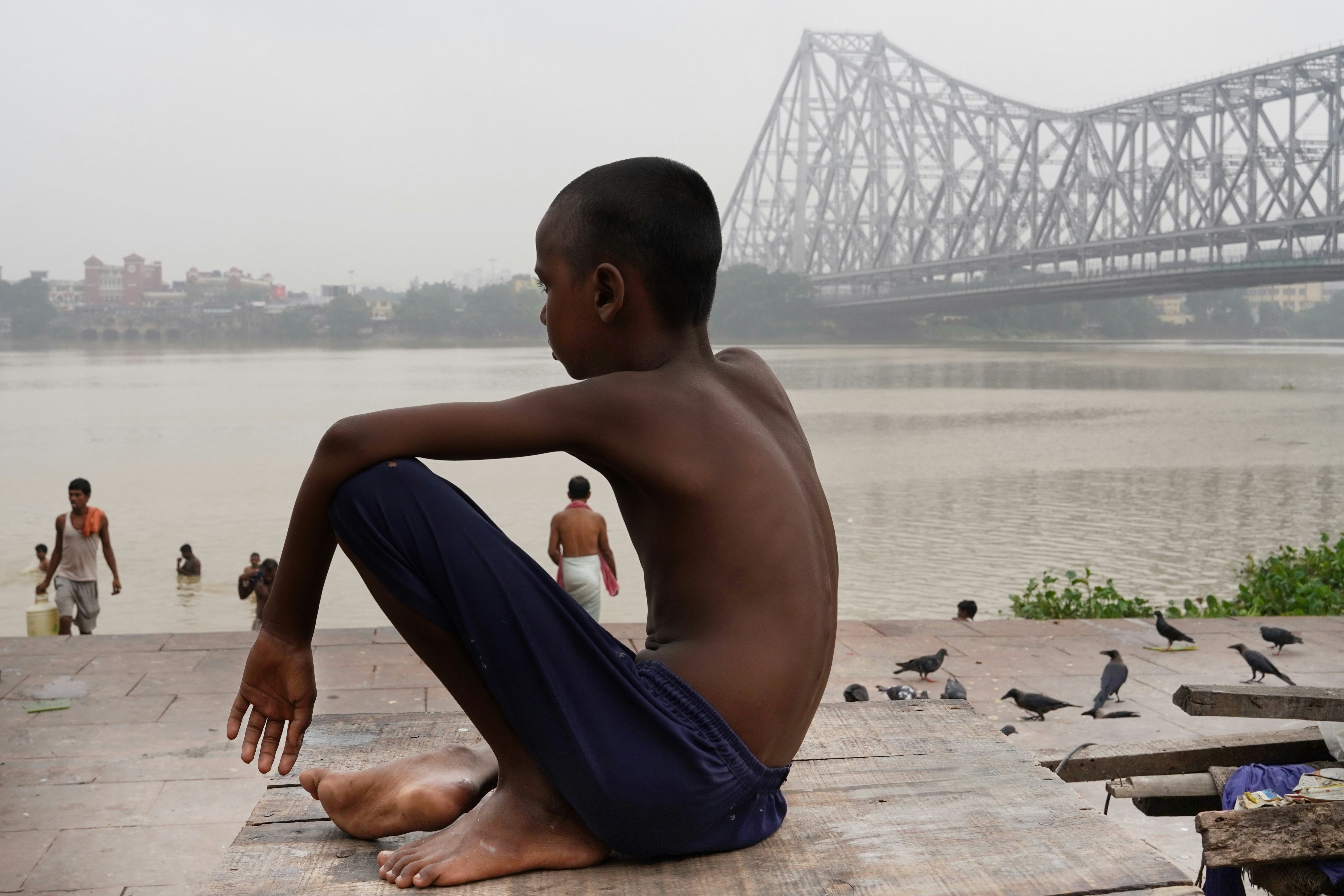 a young man sitting on the ground in front of a body of water (Photo by Dibakar Roy on Unsplash)