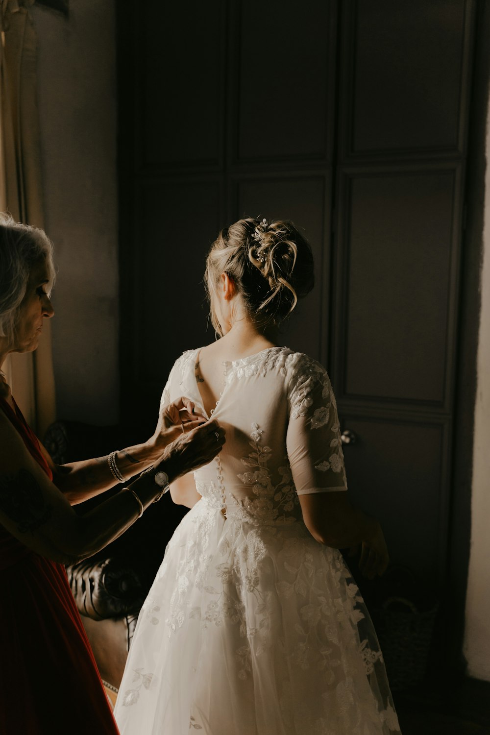 a woman helping another woman put on her wedding dress