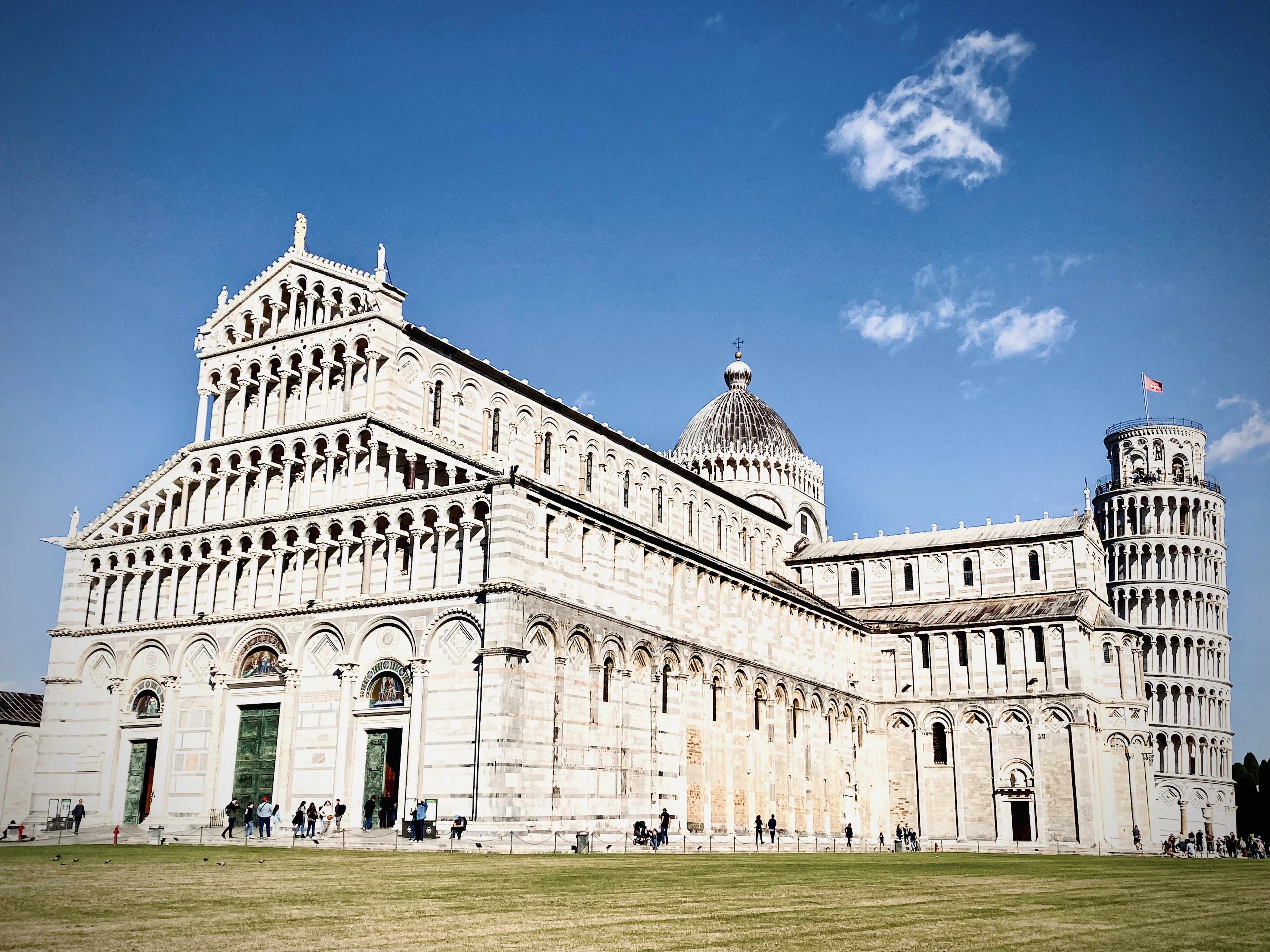 Pisa Cathedral's marble facade with the Leaning Tower rising behind it under a vivid blue sky.