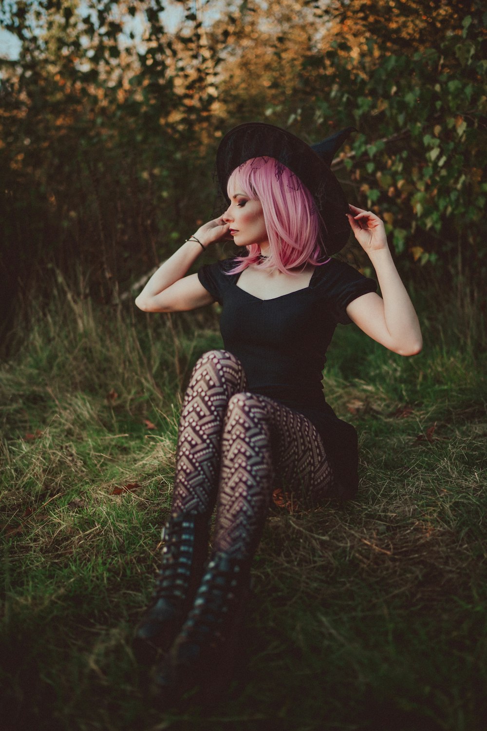 a woman with pink hair sitting in the grass