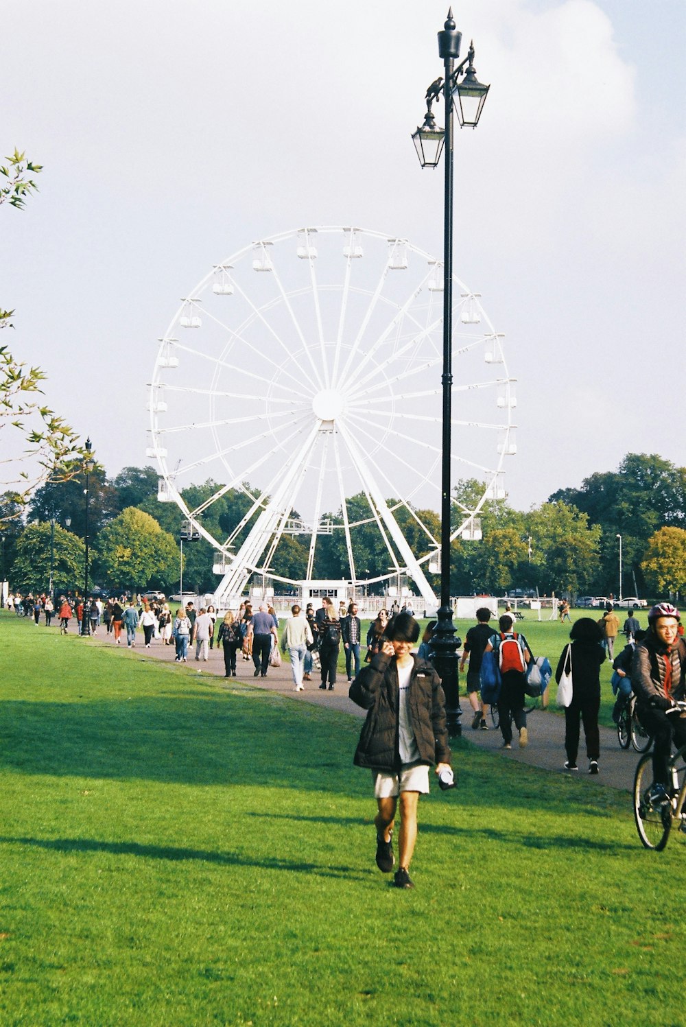 a crowd of people walking around a park next to a ferris wheel