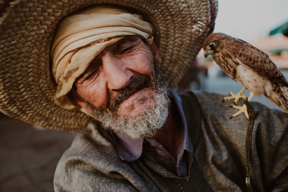 a man wearing a straw hat holding a bird on his arm