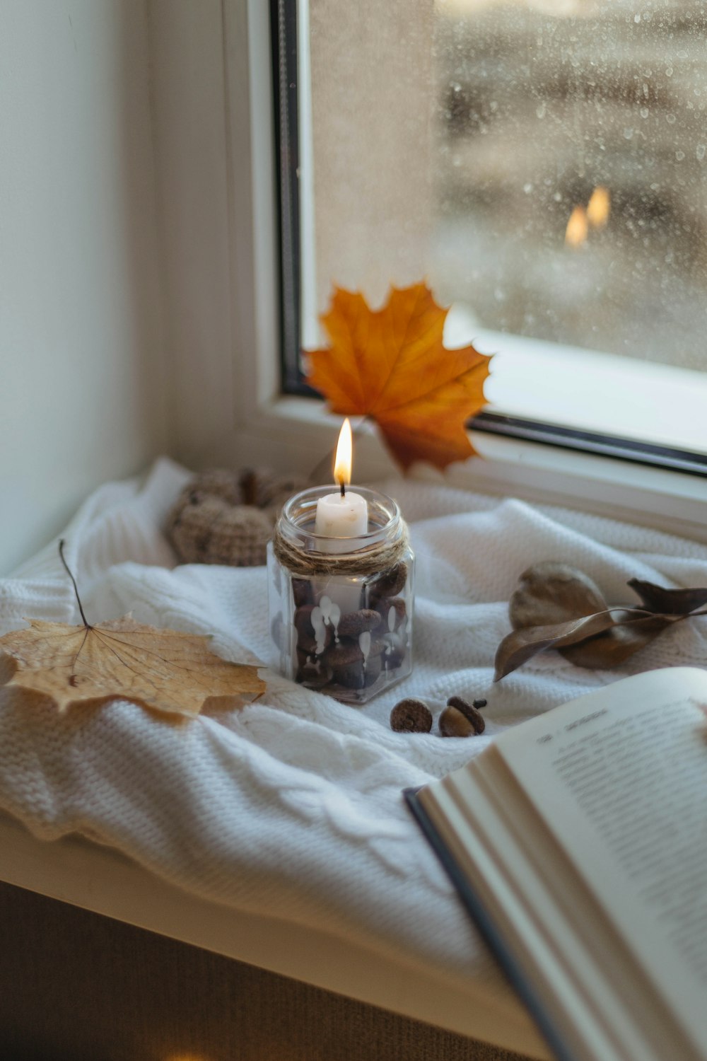 a candle sitting on top of a window sill next to an open book