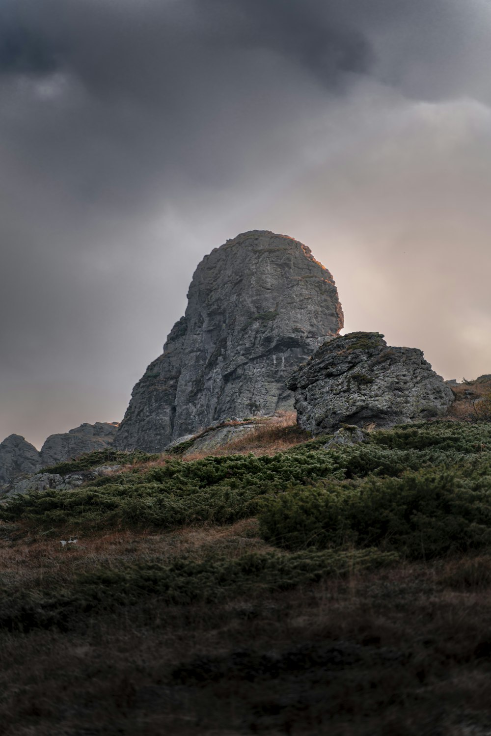 a large rock on a hill under a cloudy sky