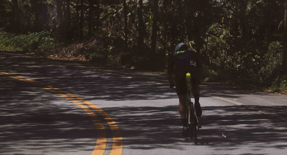 a man riding a bike down a street next to a forest