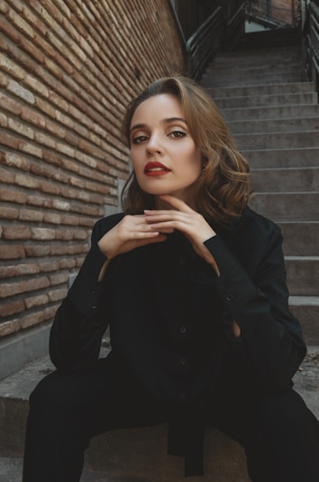 a woman sitting on the steps in front of a brick wall