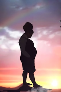 A peaceful silhouette of a mother holding her unborn baby against a soft sunrise background.