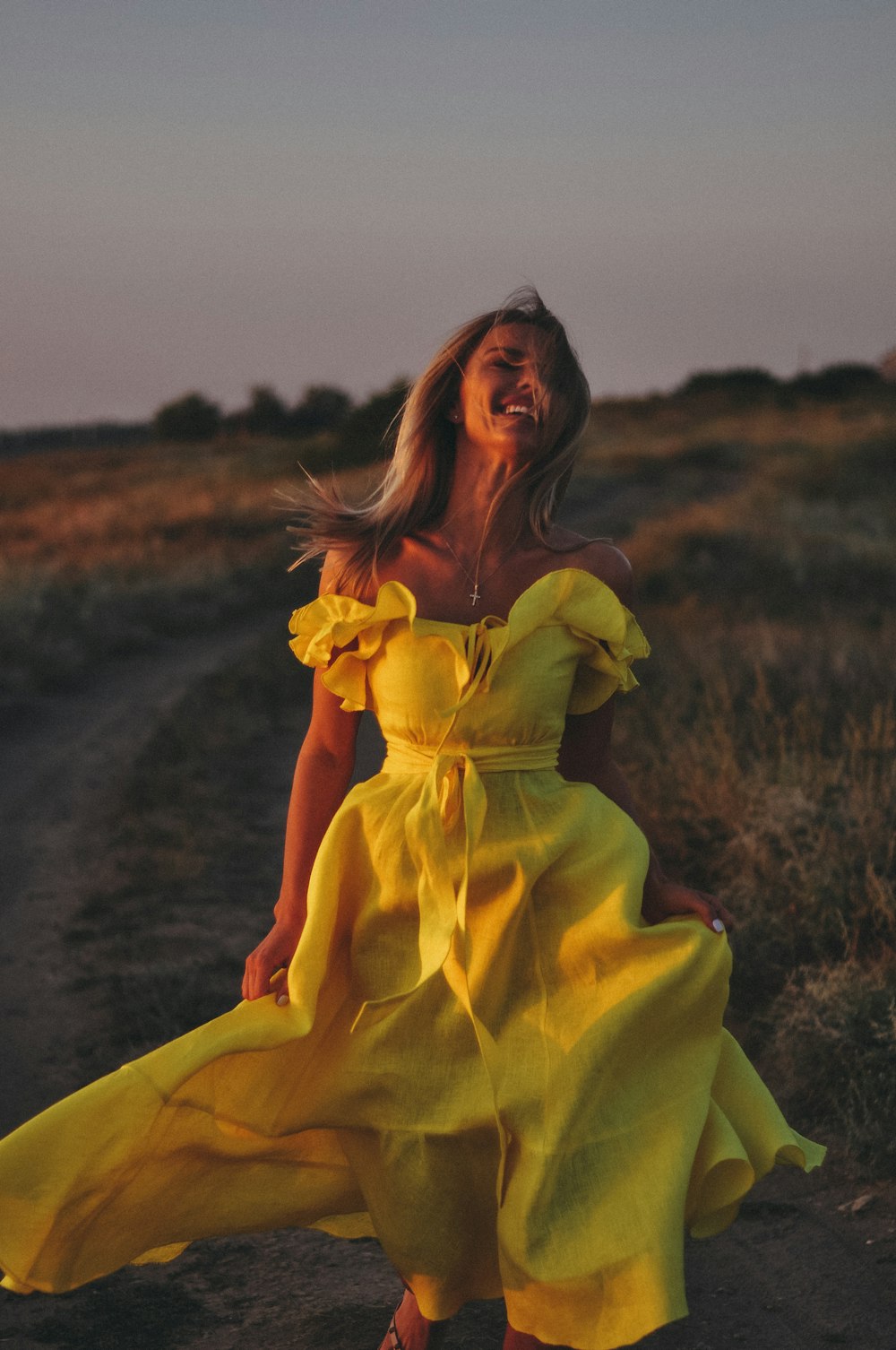 a woman in a yellow dress walking down a dirt road