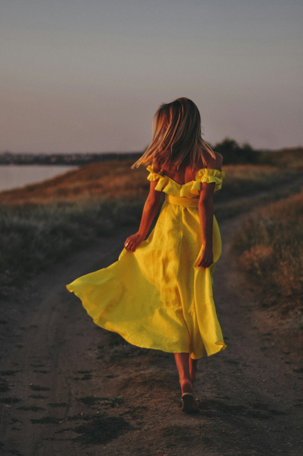 uma mulher em um vestido amarelo andando por uma estrada de terra